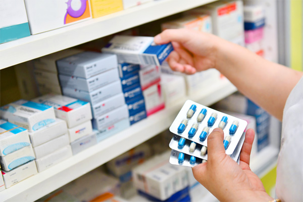 Pharmacist holding multiple bubble packs while selecting medication from shelf