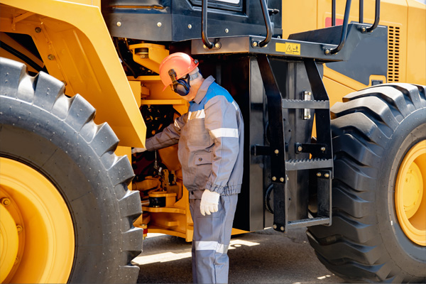 Technician performing maintenance on large road construction machinery