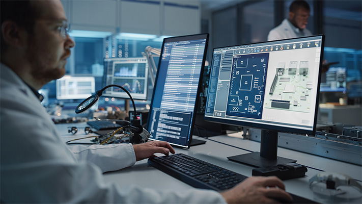 Electrical engineer reviewing PCB layout and schematic design on computer in lab