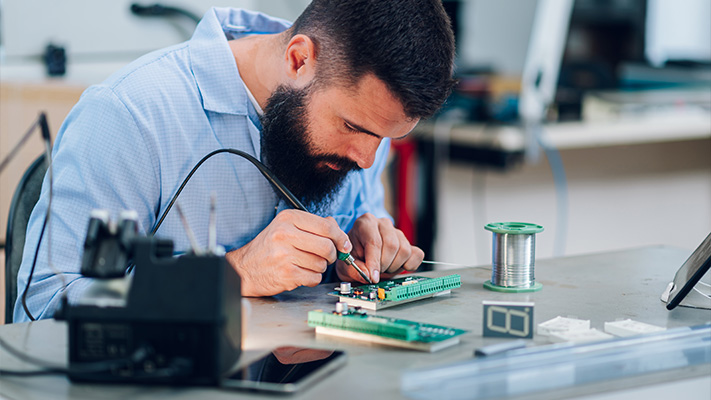 Technician soldering components onto circuit board during electronic product prototyping