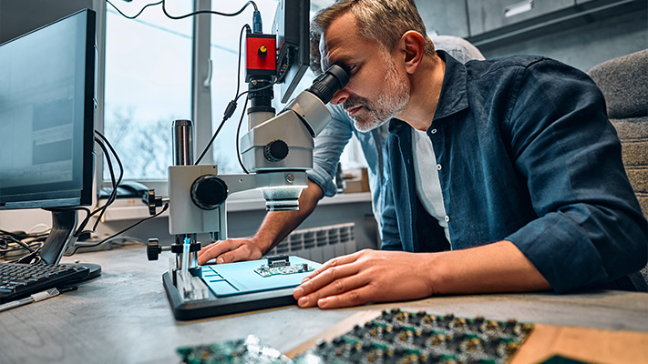 Engineer examining circuit board under microscope during product development process