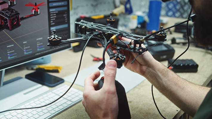 Engineer testing early-stage electronic prototype drone connected to development system