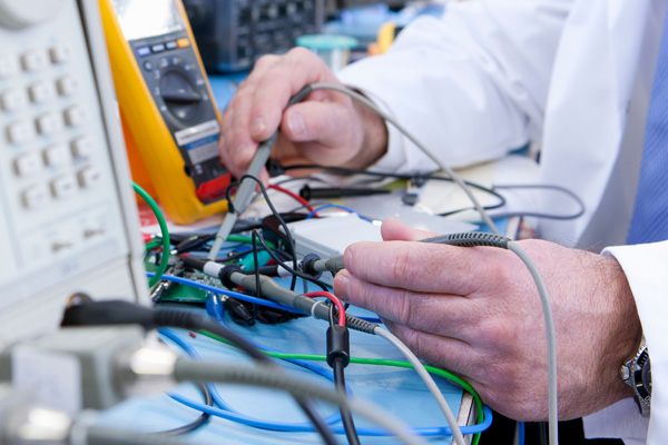 Electronics engineer probing a PCB on a test bench during compliance or insulation testing.